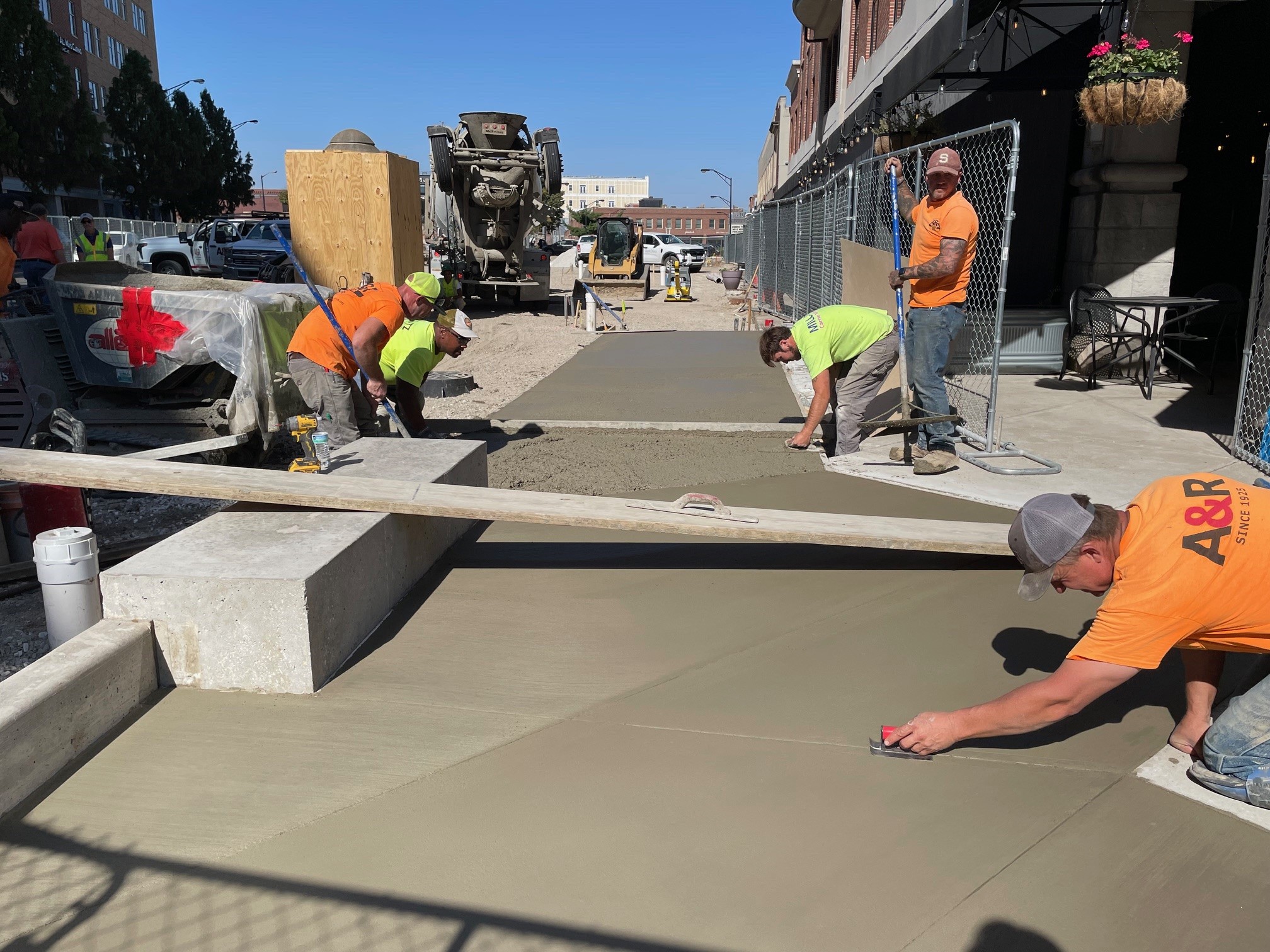 Construction workers from A&R Mechanical pour, smooth, and score concrete near Big Grove's outdoor seating area in Downtown Champaign, at the northeast corner of Neil and Main (looking north from Main).