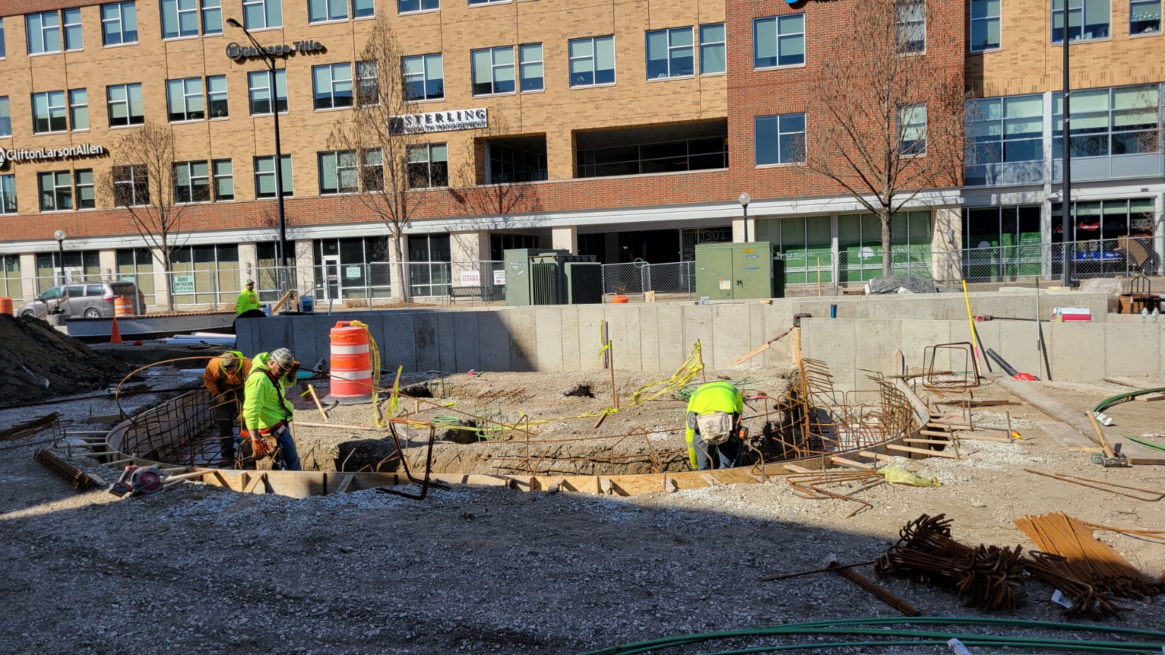 A close up photo of three construction workers installing rebar and wood to set the foundation for the stage in the downtown plaza.