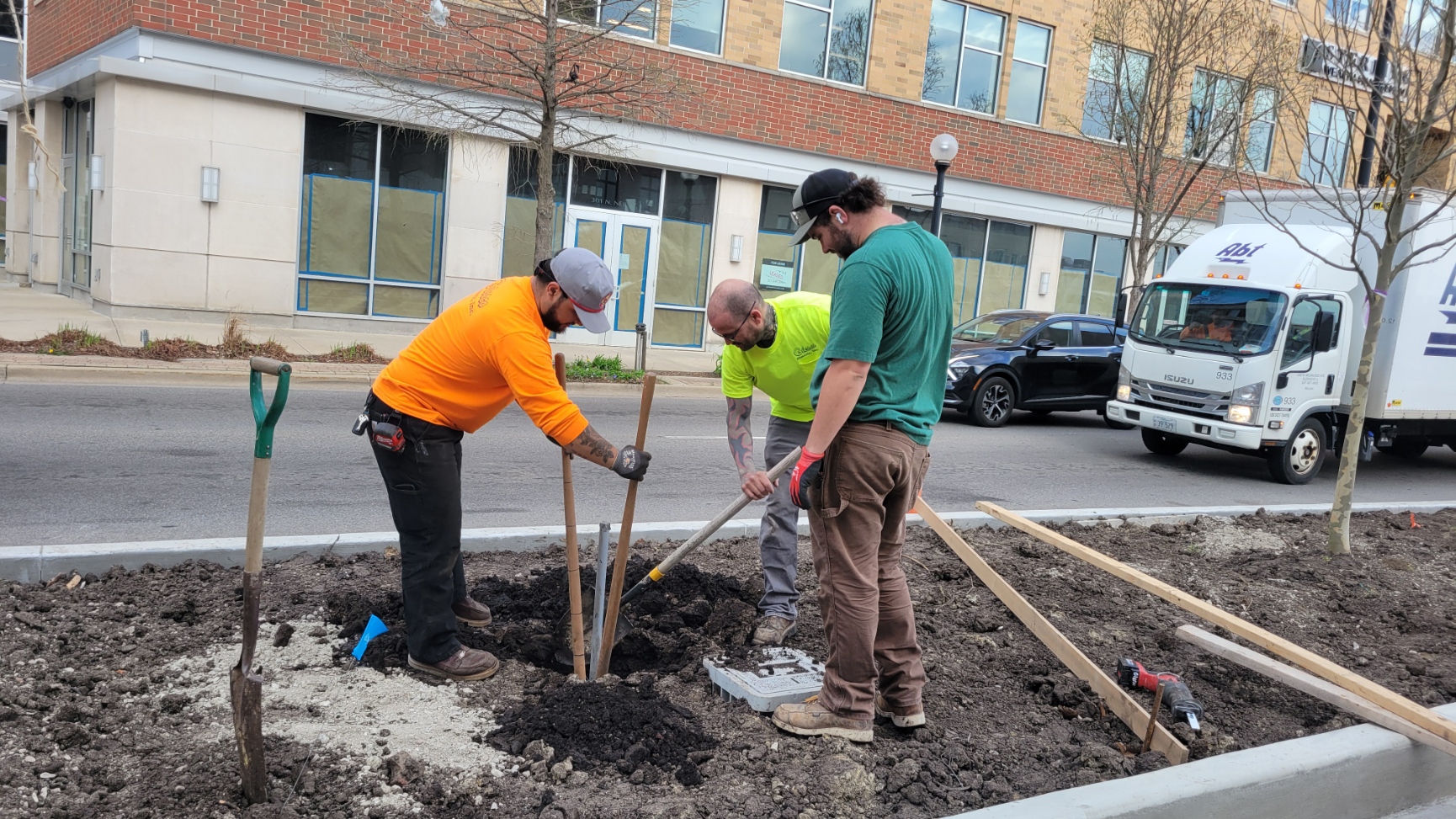 Three electrical workers actively working in a planter on the west side of the plaza to install electrical power hookups.