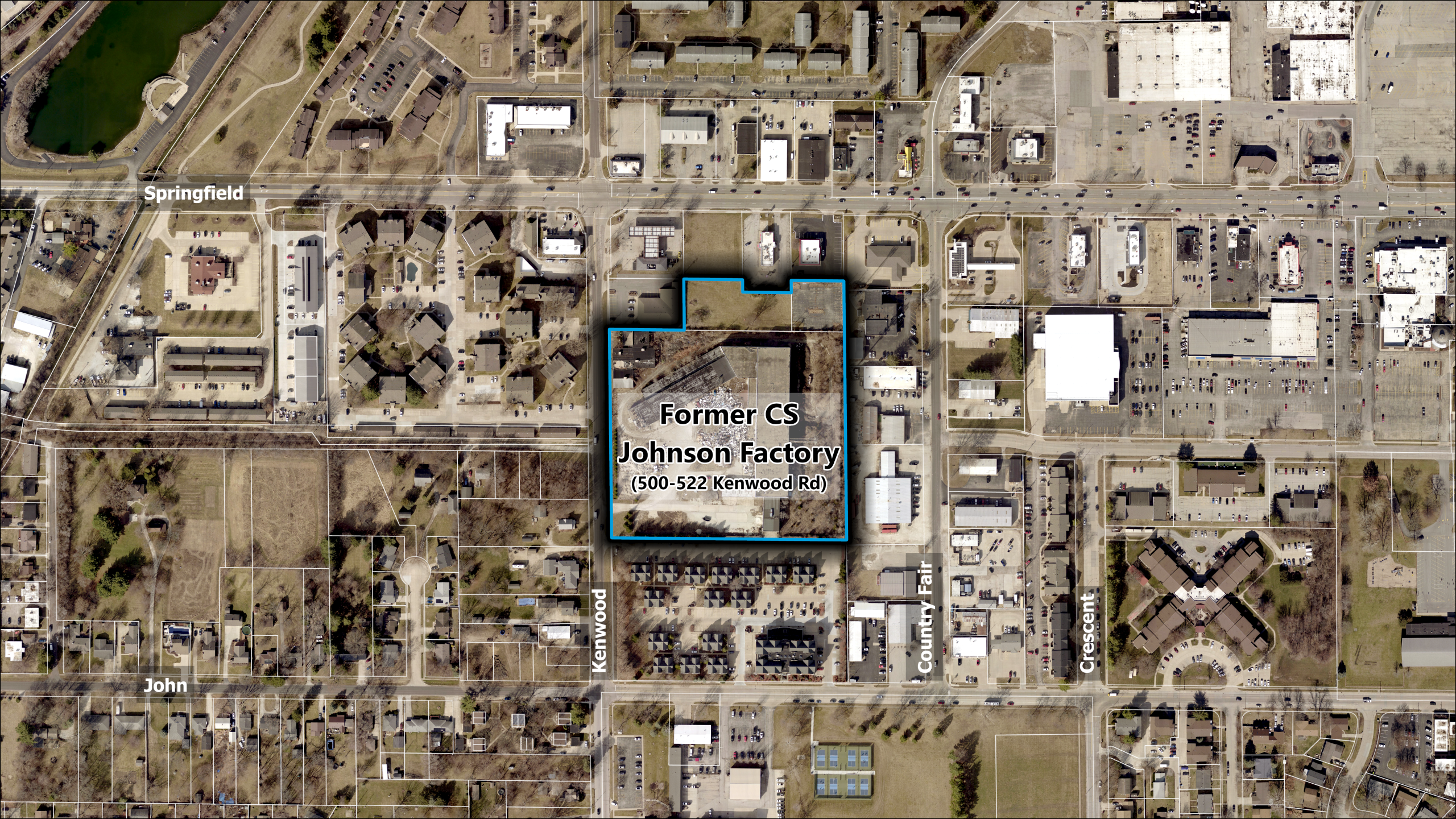 An aerial map showing tax lot lines in white and the subject property in blue. The subject property is labeled "Former CS Johnson Factory (500-522 Kenwood Rd). The subject property encompasses three lots on the east side of Kenwood Road between Springfield Avenue and John Street. One large lot has frontage on Kenwood and is where the vacant factory lies. The two other lots are immediately north of this property, much smaller than the old factory lot, and do not have street frontage (landlocked lots).