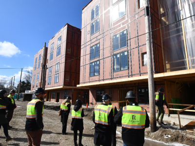 A group of people in high-visibility vests stand on a construction site in front of a building under construction.